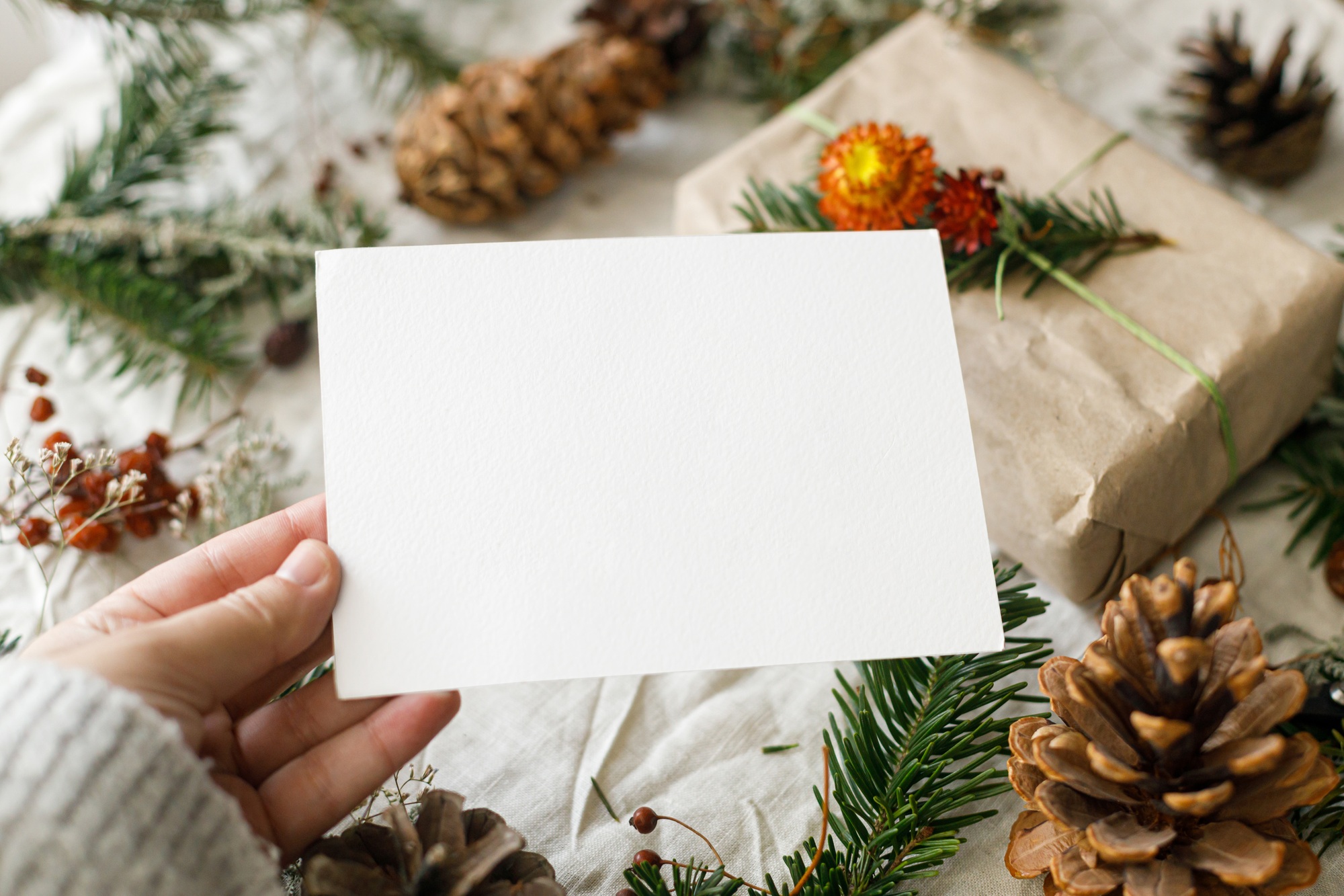 Christmas card mock up. Hand holding empty greeting card on rustic table